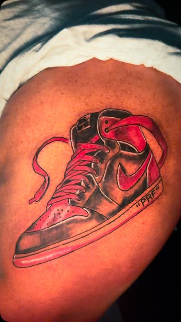 Colour tattoo of a red and black Jordan 1 sneaker on a thigh