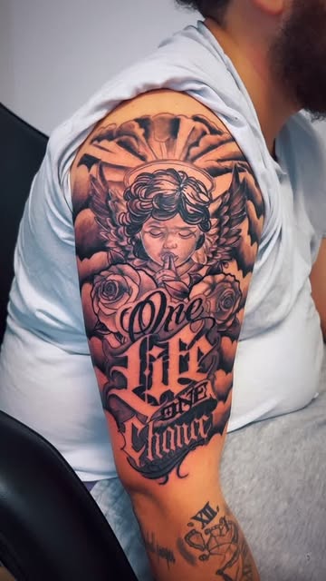 Upper arm tattoo with a cherub, roses and script reading One Life One Chance